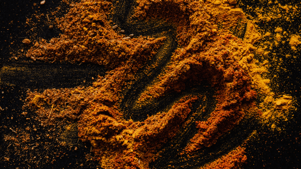Ground turmeric powder scattered on a dark surface, highlighting texture, color variation, and natural plant compounds used in plant science research